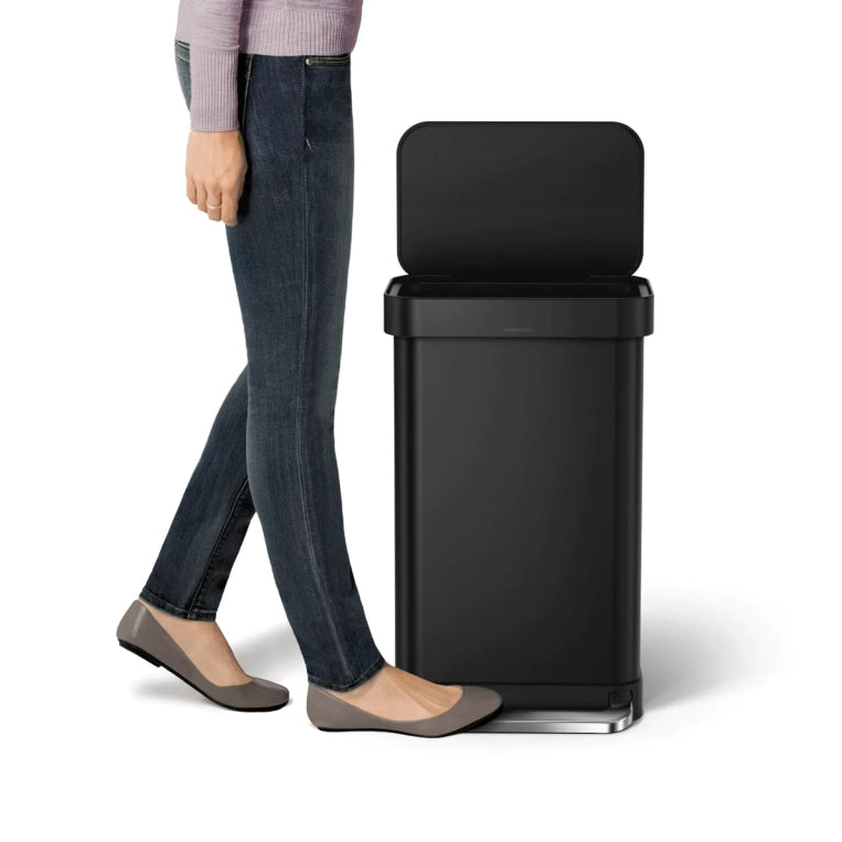 Person standing next to a black trash can on a white background