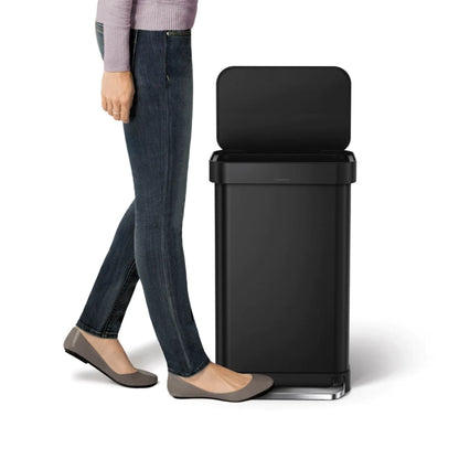Person standing next to a black trash can on a white background